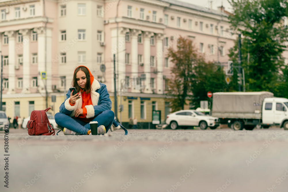 Beautiful young woman sitting outside on street together with cell phone Outdoors city background. Lifestyle