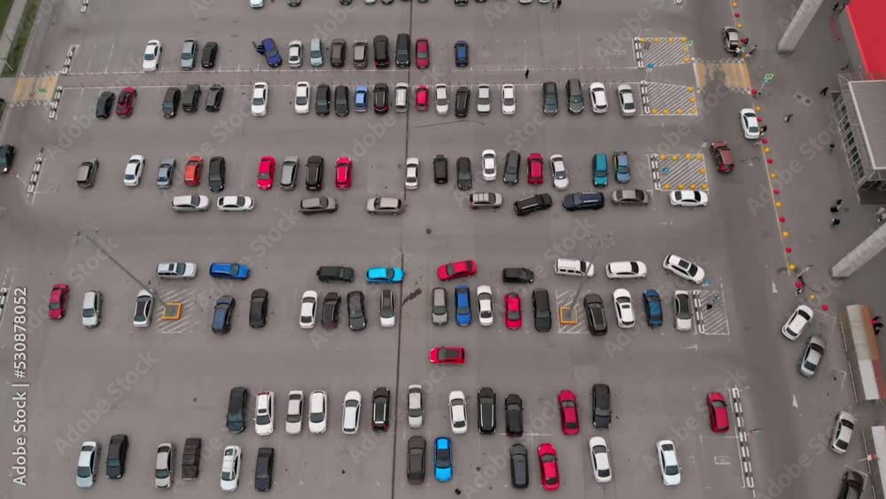 Top view of a parking lot with various cars of visitors to the mall. Multi-colored cars are parked in the parking lot from which people go shopping. Drone view of the parking lot with cars. Top view of a parking lot with various cars of visitors to the mall. Multi-colored cars are parked in the parking lot from which people go shopping. Drone view of the parking lot with cars.
