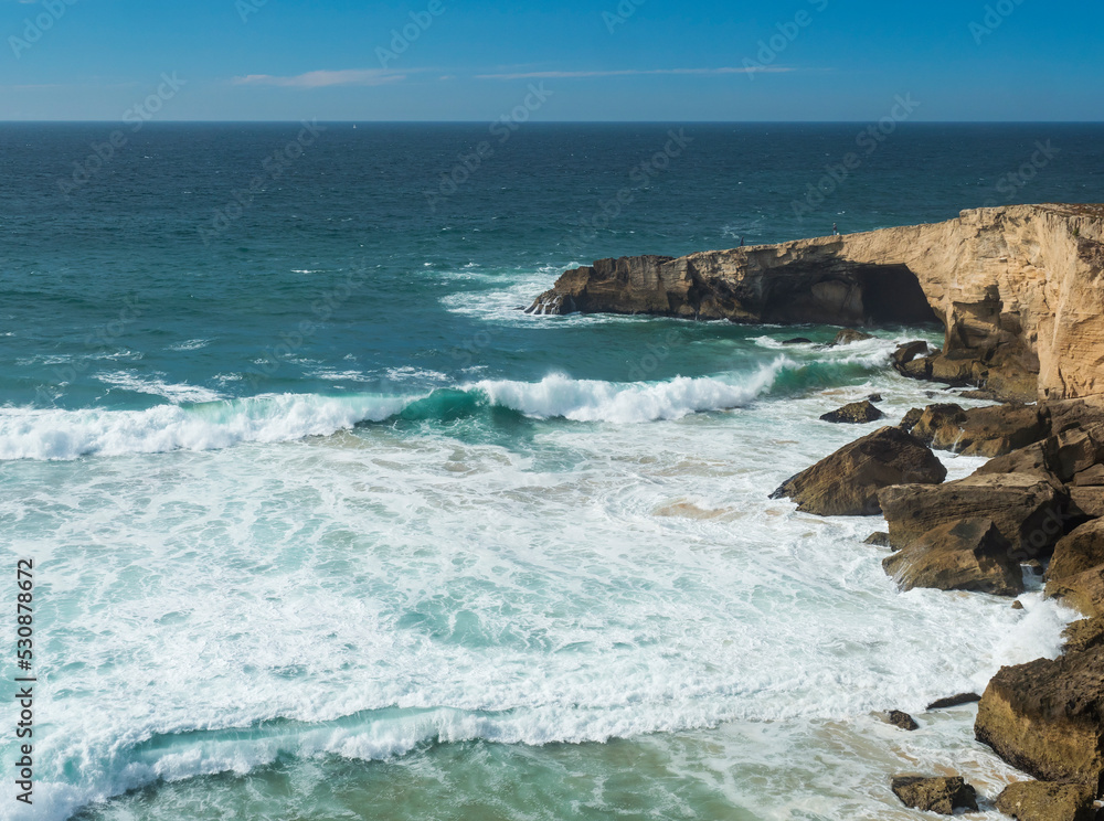 View of sharp cliffs stones and ocean waves with sea breaker foam at wild Rota Vicentina coast near Vila Nova de Milfontes, Portugal.