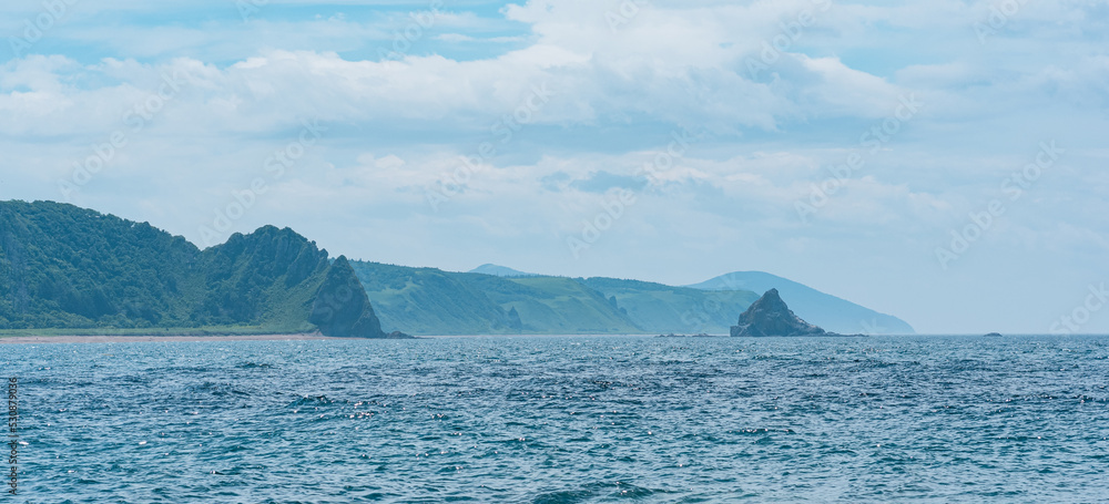 seascape with distant wooded shore with volcanic rocks, Kunashir island