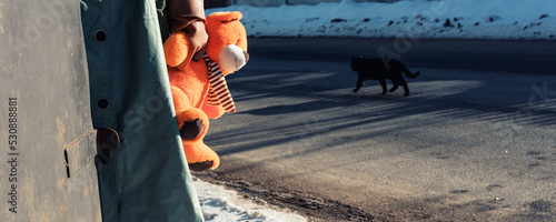 Soldier or rescuer wearing chemical clothes holds plush bear in hand against black cat walking at street