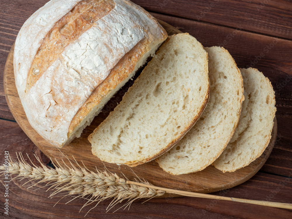 Close-up of fresh crispy wheat bread sliced lies on a wooden board. Wooden brown background. several ears of wheat are lying next to the bread. Top view, flat lay