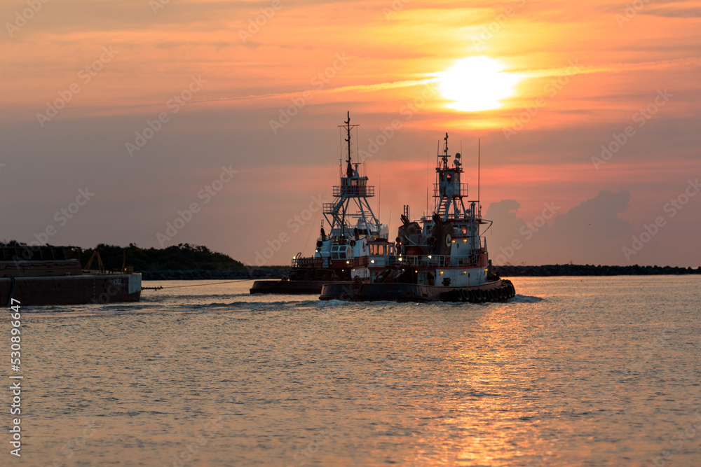 Tow Boats towing cargo through the port during sunrise. 