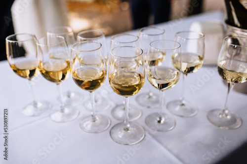 A lot, a row of glass glasses with champagne stands on the table.