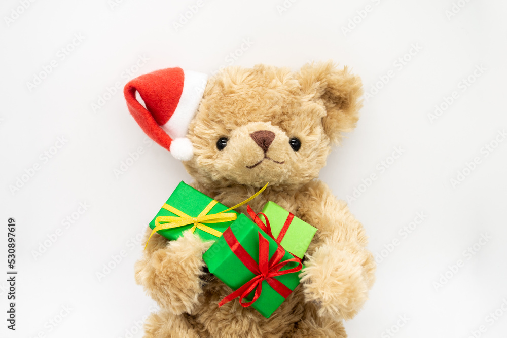 Fototapeta premium A stuffed toy Teddy bear in a red Santa Claus hat with a pompom on ear, holding green gift boxes in its paws. The concept of Christmas gifts, sales