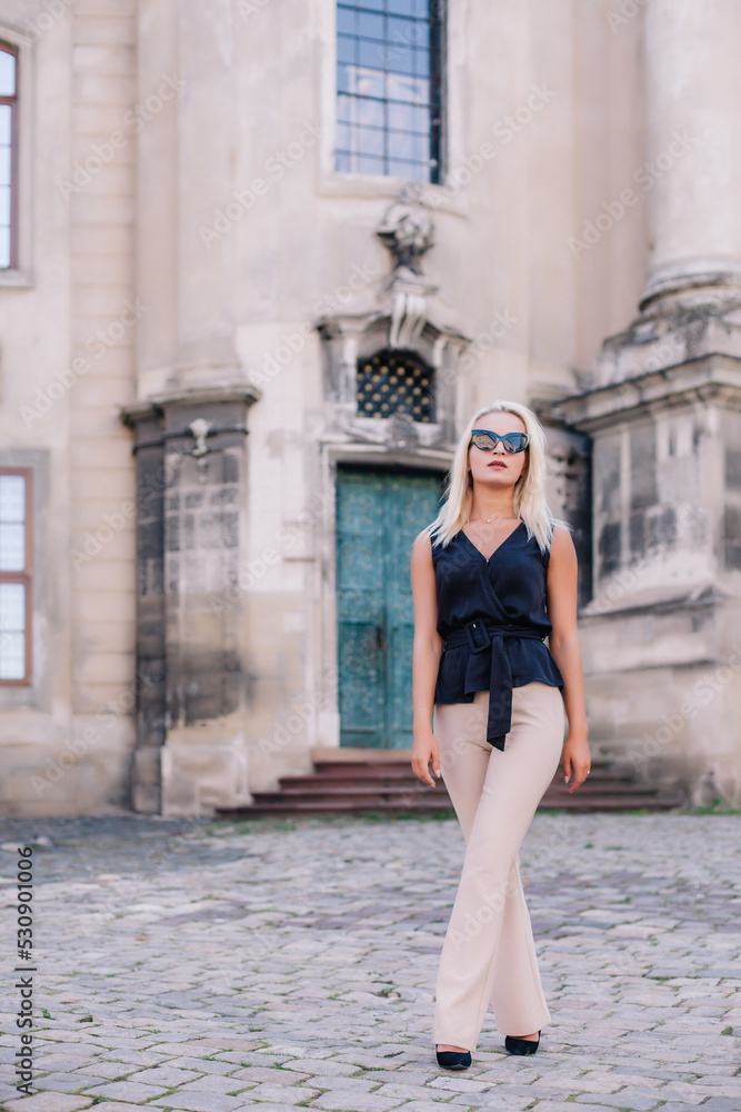 A young, blonde girl in a black blouse and sunglasses poses against the backdrop of an old courtyard in Lviv. Ukraine.