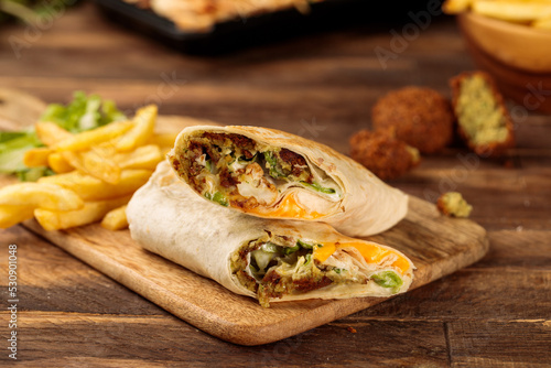 Falafel wrap shawarma with fries served in a cutting board isolated on wooden table background side view of fastfood
