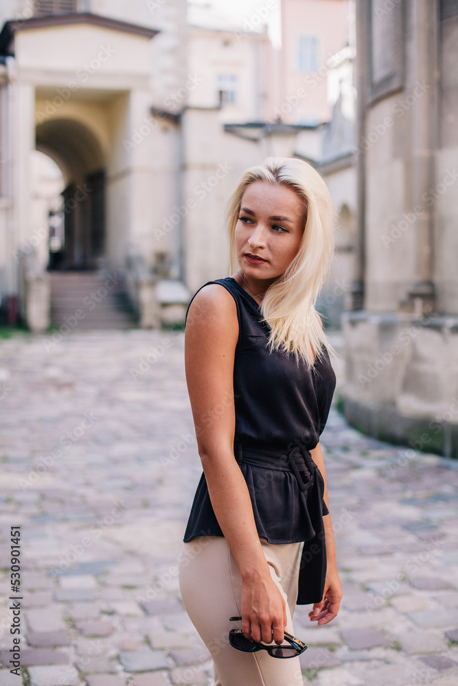 A young, blonde girl in a black blouse and sunglasses poses against the backdrop of an old courtyard in Lviv. Ukraine. A young, blonde girl in a black blouse and sunglasses poses against the backdrop of an old courtyard in Lviv. Ukraine.