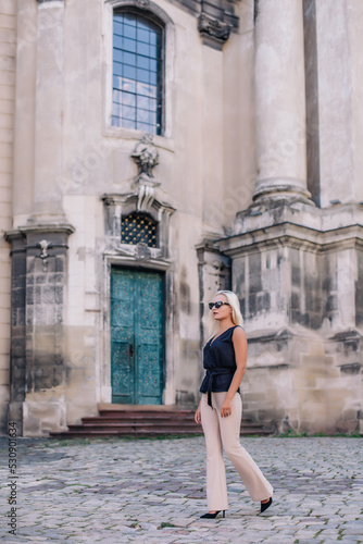 A young, blonde girl in a black blouse and sunglasses poses against the backdrop of an old courtyard in Lviv. Ukraine.