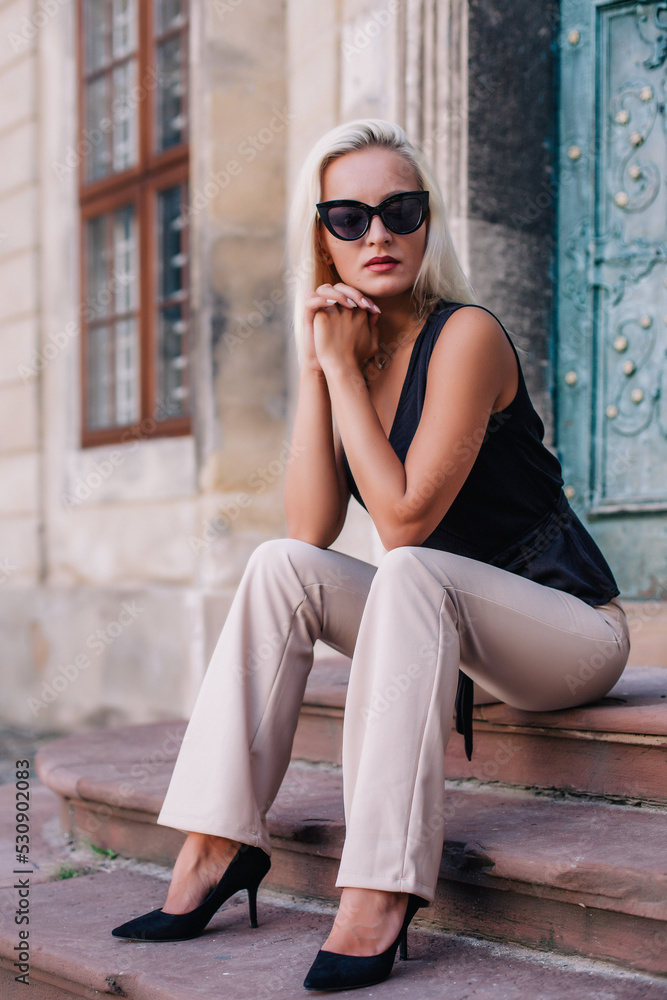 A young, blonde girl in a black blouse and sunglasses poses against the backdrop of an old courtyard in Lviv. Ukraine. A young, blonde girl in a black blouse and sunglasses poses against the backdrop of an old courtyard in Lviv. Ukraine.