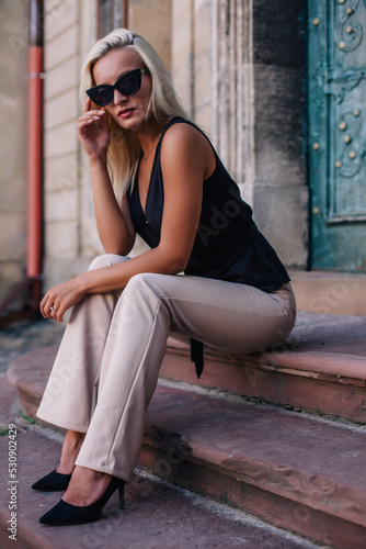A young, blonde girl in a black blouse and sunglasses poses against the backdrop of an old courtyard in Lviv. Ukraine.