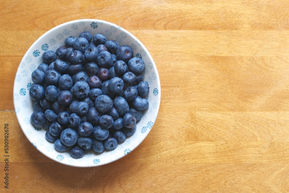Top view of fresh organic antioxidant blueberries in a white and blue porcelain bowl on a wooden table. Top view of fresh organic antioxidant blueberries in a white and blue porcelain bowl on a wooden table.
