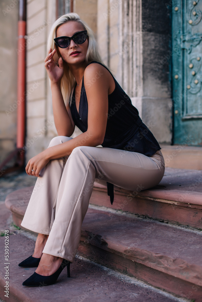 A young, blonde girl in a black blouse and sunglasses poses against the backdrop of an old courtyard in Lviv. Ukraine. A young, blonde girl in a black blouse and sunglasses poses against the backdrop of an old courtyard in Lviv. Ukraine.