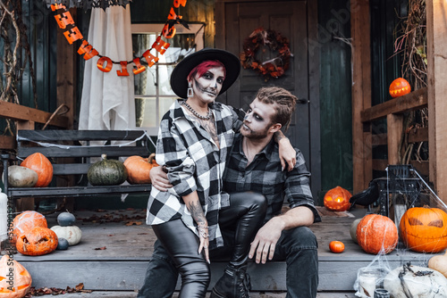 Scary love family couple man,woman celebrating halloween.Terrifying black skull half-face makeup,witch costumes.Stylish images,hat.Photoshoot,holiday party. Decorating of porch,pumpkin jack-o-lantern