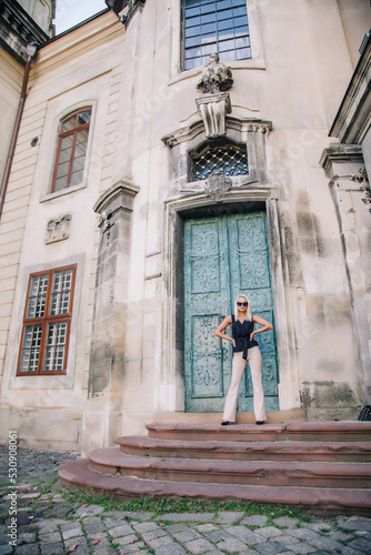 A young, blonde girl in a black blouse and sunglasses poses against the backdrop of an old courtyard in Lviv. Ukraine.