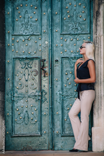A young  blonde girl in a black blouse and sunglasses poses against the backdrop of an old courtyard in Lviv. Ukraine.