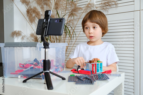 Little 5 year boy is filming his game of building constructor blocks on his smartphone. The child is broadcasting video to social networks. Kid blogger communicates with his online audience. Blogging