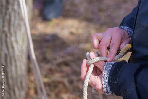 Hands of a tourist tying knots on a rope with selective focus. Background with copy space
