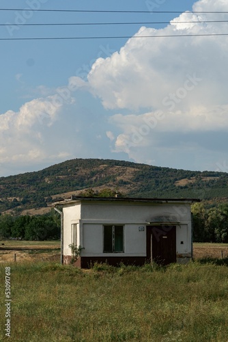 Vertical shot of a hut  on a green field with a hill in the background under a cloudy sky photo