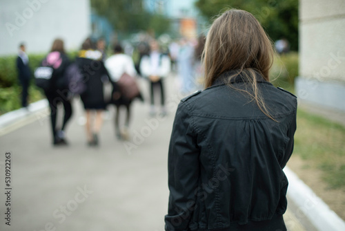 Girl in black jacket in schoolyard. Girl is coming home from school. Black clothes.