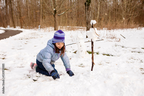 A little girl builds snowmen near path through woods in winter photo