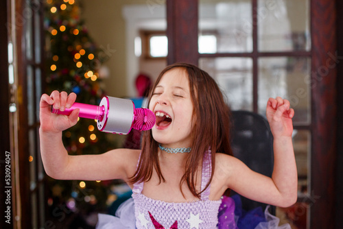 A girl in costume sings into a microphone by Christmas tree photo