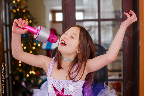 A girl with a pink microphone and tutu joyfully sings alone