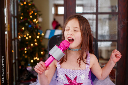 a little girl in costume sings loudly into a microphone at home photo