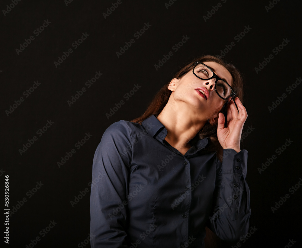 Beautiful thinking serious business woman looking up and scratching her head and deciding riddle in blue shirt on black background with empty copy space for text. Closeup Beautiful thinking serious business woman looking up and scratching her head and deciding riddle in blue shirt on black background with empty copy space for text. Closeup