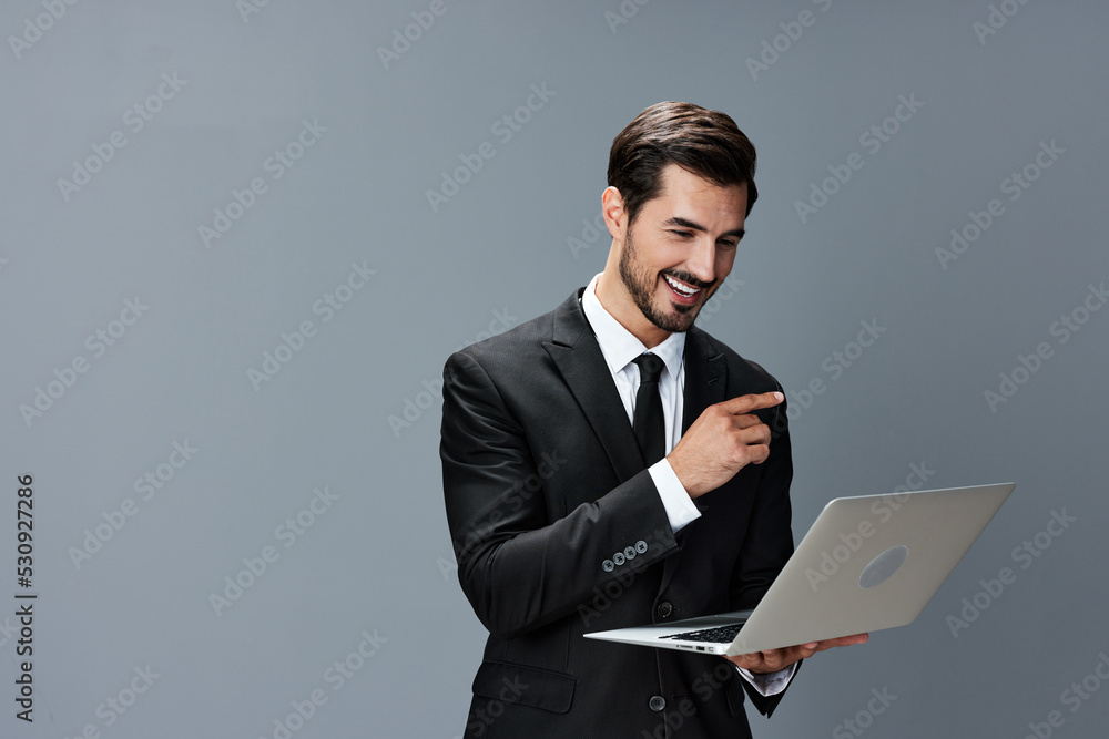 Man business stares at laptop and works thoughtfully online smiling over the internet in business suit video call business talks on gray background copy place Man business stares at laptop and works thoughtfully online smiling over the internet in business suit video call business talks on gray background copy place