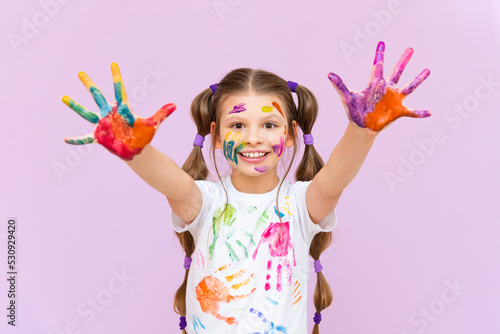A little girl painted with multicolored paints will playfully have to create on a pink isolated background. Development of children s creativity for schoolchildren.