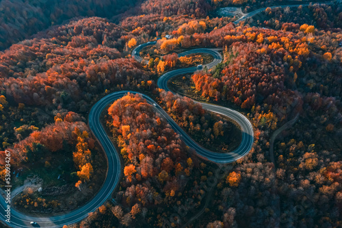 aerial photography of curved road on autumn, beautiful curved pass with vehicles and colorful autumn nature colors on trees with sunset light