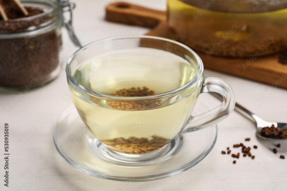 Buckwheat tea in glass cup and granules on white wooden table, closeup