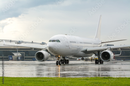 An unmarked white passenger jet on an airport apron. White plane in the parking lot at the terminal during the rain. Commercial passenger air transportation