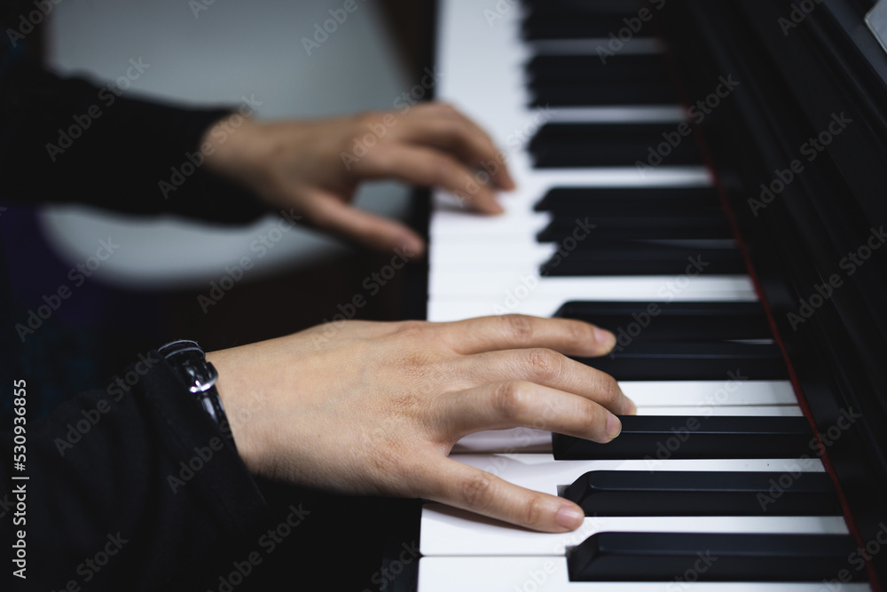 Fototapeta premium Close up of woman's hands playing piano by reading sheet music. Dark mood.
