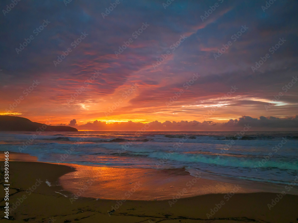 Cloud covered sunrise at the seaside in pink and blue