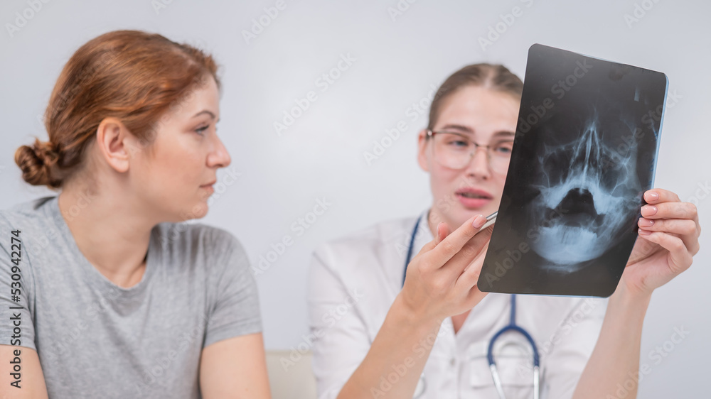 A woman doctor and a patient at the reception are discussing an x-ray of the sinuses. A woman doctor and a patient at the reception are discussing an x-ray of the sinuses.