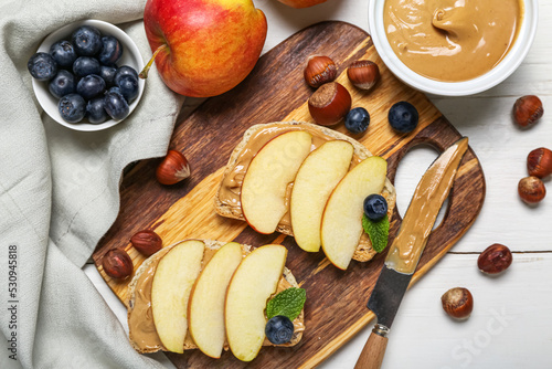 Board of tasty sandwiches with nut butter, apples, hazelnuts and blueberry on light wooden background, closeup