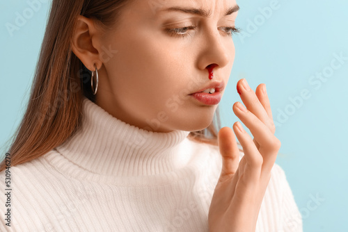Young woman with nosebleed on blue background, closeup