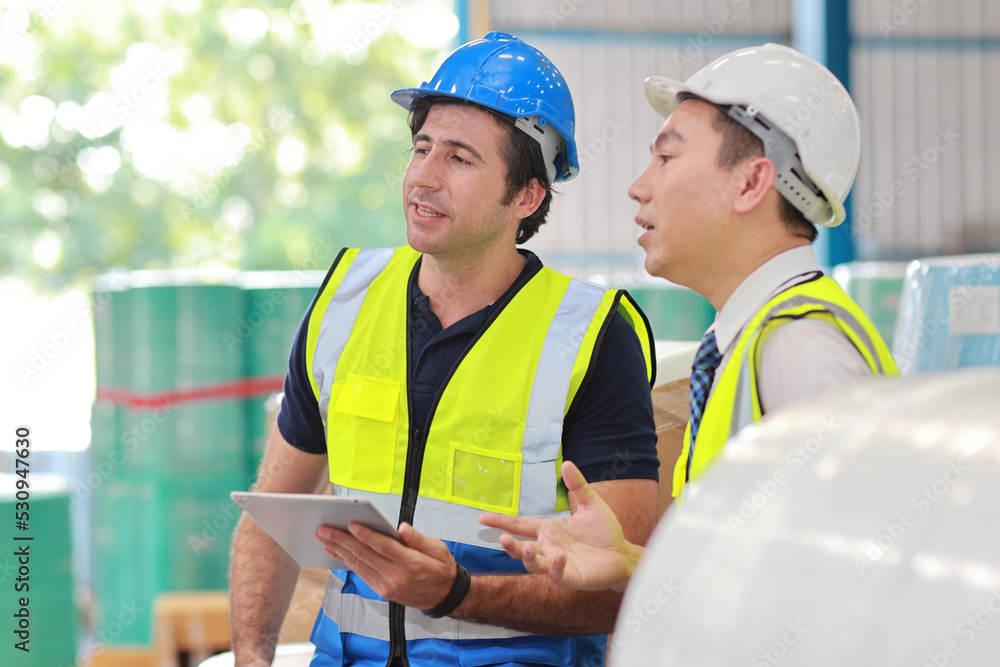 Architect or engineering men and worker standing and checking large warehouse with tablet. Multiethnic two business manager controlling work at warehouse industry building. Architect or engineering men and worker standing and checking large warehouse with tablet. Multiethnic two business manager controlling work at warehouse industry building.