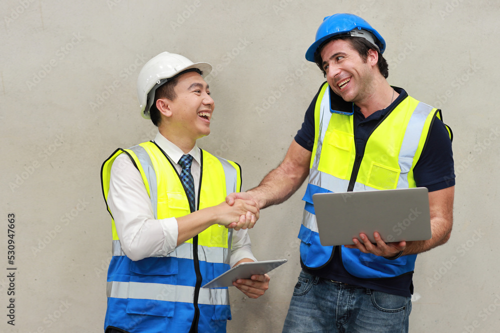 Two technician engineer man in protective uniform with hardhat standing and shaking hands celebrate successful together or completed deal commitment at industry warehouse manufacturing factory Two technician engineer man in protective uniform with hardhat standing and shaking hands celebrate successful together or completed deal commitment at industry warehouse manufacturing factory