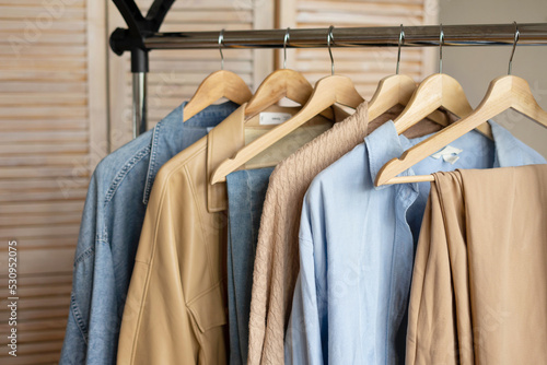 Trendy capsule wardrobe in beige and light blue on a rail rack against the backdrop of a screen.