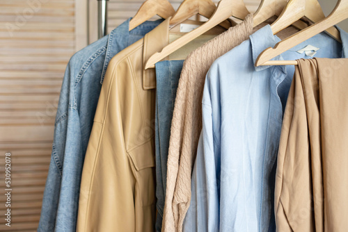 Trendy capsule wardrobe in beige and light blue on a rail rack against the backdrop of a screen.