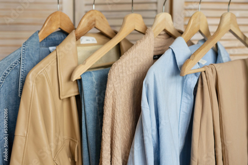 Trendy capsule wardrobe in beige and light blue on a rail rack against the backdrop of a screen.