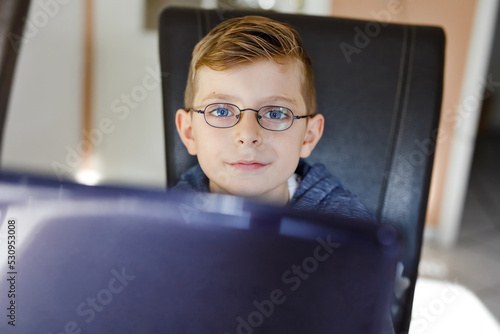 Happy healthy kid boy with glasses making school homework at home with notebook. Interested child writing essay with helping of internet. concetrated schoolchildren concept photo