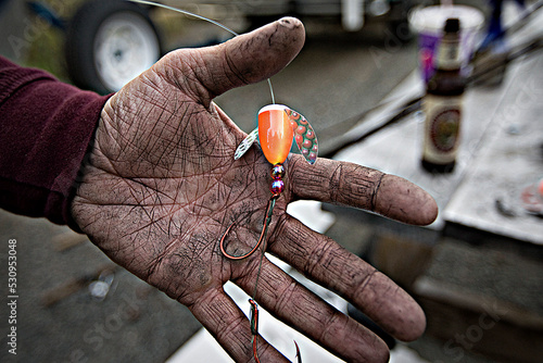 Filthy dirty hand of a fisherman holding a fishing lure with a sharp hook 