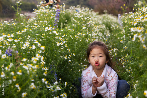 An Asian girl with a white cloth is sitting in the white flower garden making a pig's mouth.