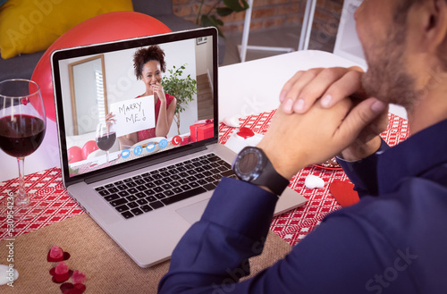 Diverse couple making valentines date video call the woman on laptop screen holding marry me sign