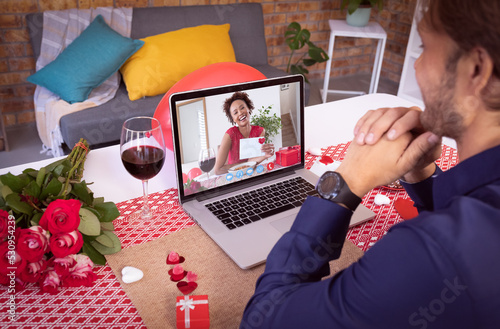 Diverse couple making valentines date video call the woman on laptop screen holding a card