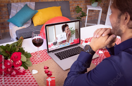 Diverse couple making valentines date video call the woman on laptop screen holding i do sign